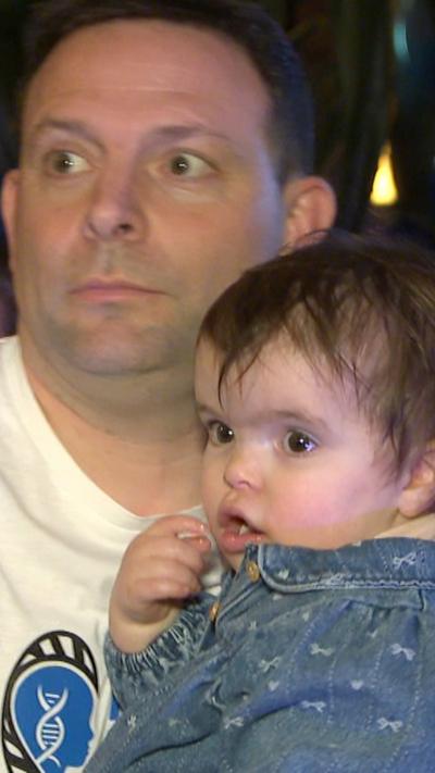 Close up of dark haired man carrying toddler girl indoors
