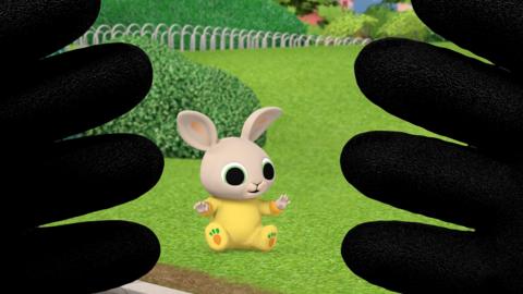 Charlie, a pale baby rabbit, sitting on the lawn. Bing's hands show he's playing peek-a-boo, covering the viewer's perspective.