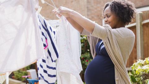 A young pregnant black woman puts out washing on washing line on a sunny day in a garden