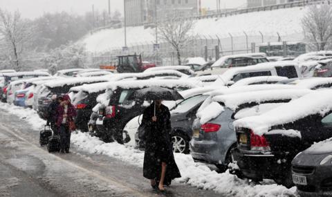 Woman walking through a car park in heavy snow carrying an umbrella