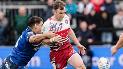 Wigan Warriors' Harry Smith (centre) kicks the ball during their Challenge Cup game at Wakefield as an opposing player tries to make a tackle