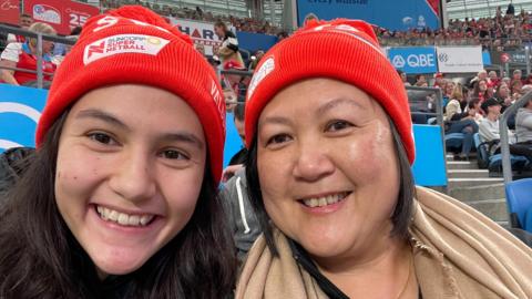 Sophie Fawns with her mother, Maureen, both smiling and wearing NSW Swifts red woolly hats