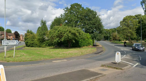 A curved road with a sign reading Stourbridge A451 to the left and cars to the right. There are road markings in the middle and trees either side.