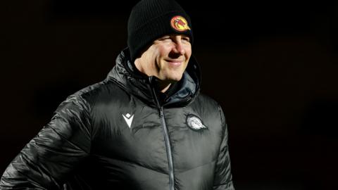Departed Catalans Dragons head coach Joel Tomkins in club emblazoned hat and coat