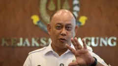 Kepala Badan Gizi Nasional (BGN) Dadan Hindayana nampak sedang bicara karena bibirnya sedikit maju, sambil mengangkat tangan kirinya. Di belakangnya terdapat latar bertuliskan kejaksaan agung.