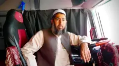 نور محمد در ماشین نشسته و دستش را به فرمان تکیه داده است