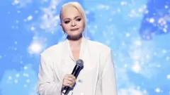 Долина c микрофоном на сцене с грустным лицом