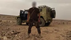 A Wagner soldier stands in front of an armoured vehicle