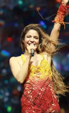 Shakira cantando em um palco, com um dos braços levantados. 