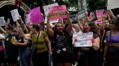 Grupo de mulheres levantando cartazes durante manifestação contra o feminicídio em dezembro de 2025.