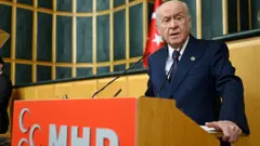 Devlet Bahçeli kürsüde konuşurken, üzerinde koyu renkli bir takım elbise var