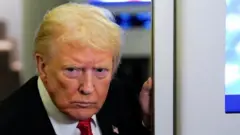 US President Donald Trump looks on as he speaks to members of the media on board Air Force One.
