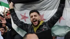 सिरियाली झण्डा फहराएर उत्सव मनाउँदै भिडमा एक मानिस