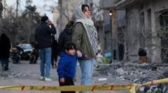 زنی به همراه فرزندش به ویرانی در اثر حمله هوایی اسرائیل و آمریکا به یک ایستگاه پلیس نگاه می‌کند، ۲ مارس ۲۰۲۶