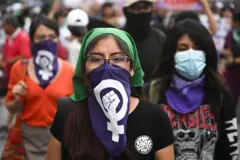 Women wearing a green headscarf and a blue scarf covering her mouth, surrounded by other women at a protest in Lima, Peru