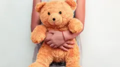 Vista da cintura de uma menina segurando seu ursinho de pelúcia.