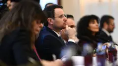 Odakta gürlek var dikey uzanan bir masada sağında ve solunda odak dışında resmi giyimli kadınlar. 