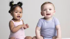 A baby girl in a pink baby grow and and baby boy in a blue baby grow