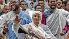 A crowd, including a woman in a traditional white shawl who plays a huge painted drum, sing New Year songs at Entoto St Raguel Church in Addis Ababa in Ethiopia - Thursday 11 September 2025.