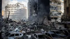 ৮ এপ্রিল, ২০২৬ তারিখে বৈরুতে ইসরায়েলি বিমান হামলার পর একটি ভবন জ্বলতে থাকার সময়, একজন দমকলকর্মী বিধ্বস্ত গাড়িগুলোর মাঝ দিয়ে হেঁটে যাচ্ছেন।