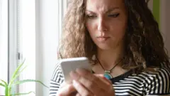 A woman looking at her phone with a cross expression on her face