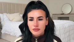 Miller yicaye, inyuma ye hari igitanda gishashe n;akabati gateretseho indorerwamo.