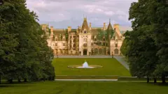 Vista panorâmica de Biltmore House, atrás de um grande jardim com árvores e uma fonte no centro
