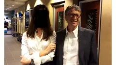 Bill Gates, con saco y camisa, posa junta una mujer con camisa blanca en un pasillo de un edificio