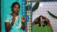 Şilpa əlində Devadasilərin taxdığı boyunbağını tutub. O, kameraya neytral bir ifadə ilə baxır. Əynində firuzəyi sari var.