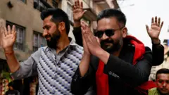 Rabi Lamichhane waves at a crowd as he stands next to Balendra Shah whose hands are clasped in front of his face