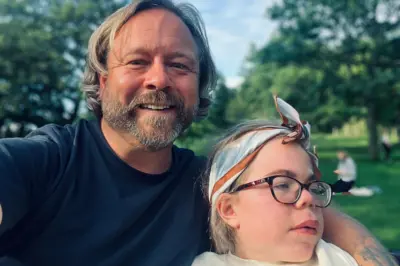 Darren y Sophia Scott. Él tiene el cabello rubio, algo largo, y barba, y lleva puesta una camiseta azul. Tiene el brazo alrededor de Sophia, quien lleva gafas y una bufanda de algodón azul, marrón y blanca atada alrededor de la cabeza. Él sonríe a la cámara, mientras que ella mira hacia fuera de cuadro. Se encuentran en un parque.