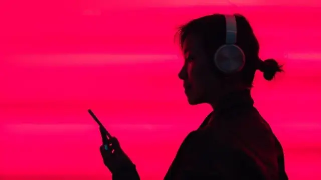 Телефонига қараб қулоқчинда нимадир эшитаётган осиёлик аёл