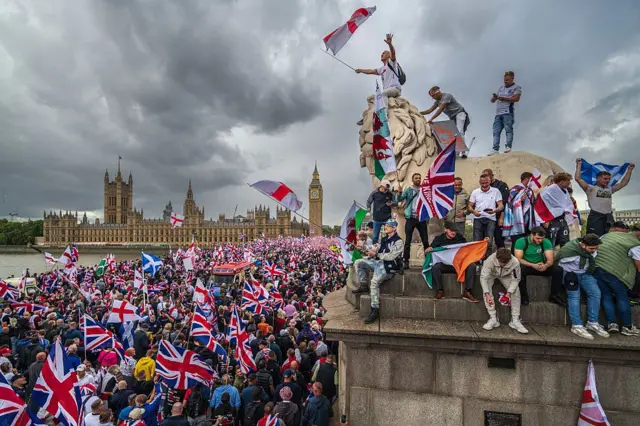 More than 110,000 people gathered in central London, where protesters are seen holding UK flags with the Parliament in the background. මධ්‍යම ලන්ඩනයේ 110,000කට අධික පිරිසක් රැස්ව සිටි අතර, විරෝධතාකරුවන් එක්සත් රාජධානියේ ධජ අතැතිව පාර්ලිමේන්තුව පසුබිමේ තබාගෙන සිටිනු දක්නට ලැබුණි