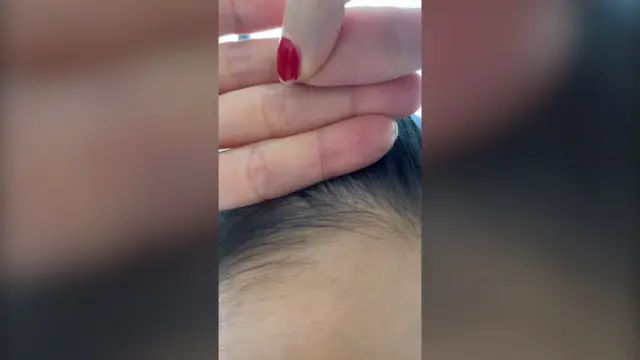 মারিয়ার একটি চুল উপরের দিকে ধরে আছেন; যেখানে চুলের গোড়া অংশটি গাঢ় রঙের এবং ডগার দিকটি রুপালি দেখা যাচ্ছে।