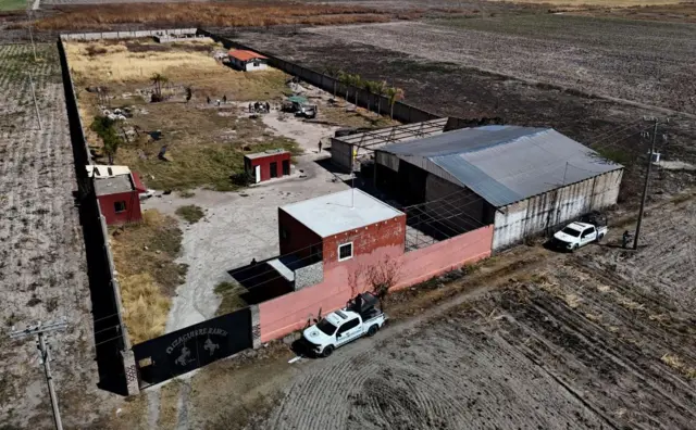 Rancho Izaguirre, sebuah kompleks berpagar dengan bangunan tambahan, dikelilingi ladang yang dibajak dan dipagari tiang telepon