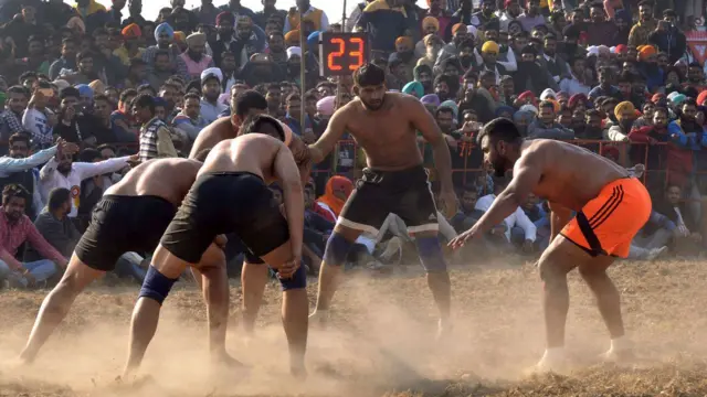 Baba Suckhchain Dass Kabaddi Shahkot (R) attempts to tag an Dashmesh Kabaddi Club Nakodar opponent during the first Kabaddi Cup Tournament in Amritsar on February 5, 2016. Five men wearing shorts and some wearing knee grips lean in to a scrum formation at a dusty sports ground watched by a big audience. 