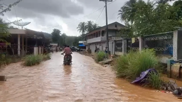 Seorang pengendara sepeda motor sedang menerjang air banjir.