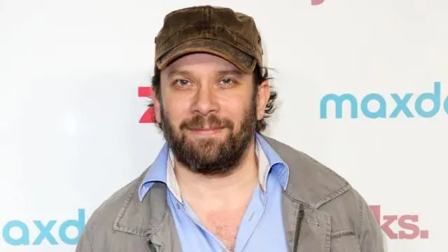 Sakallı ve şapkalı bir adam kameraya bakıyor