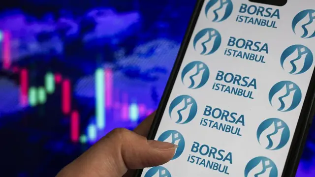 Arka plandaki mum grafiklerinin önünde bir kişinin elinde tuttuğu telefonda Borsa İstanbul logoları yer alıyor