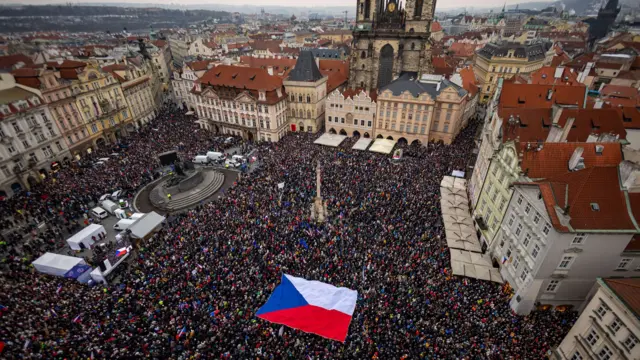 Вид згори на площу в Празі, повний людей з розтягнутим прапором Чехії