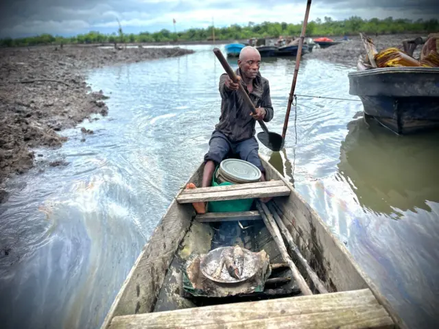 Birabi Nenage dey paddle canoe close to shore in K-Dere community. E get slicks of oil on di river wia e dey paddle.