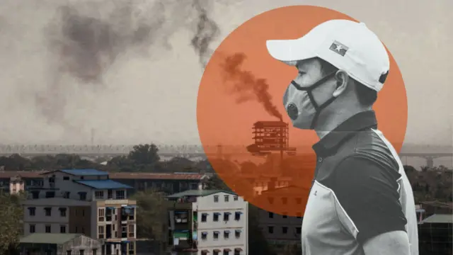 ရန်ကုန်မြို့က စက်ရုံတစ်ခုရဲ့ မီးခိုးခေါင်းတိုင်ကနေ မီးခိုးလုံးတွေ ကောင်းကင်ကို ထိုးတက်နေတဲ့မြင်ကွင်း၊ အထပ်မြင့်တိုက်အချို့နဲ့ အနောက်ဘက် ခပ်ဝေးဝေးမှာ မြစ်ကူးတံတား တစ်စင်းကို မြင်တွေ့ရ၊ ဓာတ်ပုံအရှေ့ပိုင်းမှာတော့ ဘယ်ဘက်ကို လှည့်နေတဲ့ လျှာဦးထုပ်အဖြူဆောင်းထားပြီး၊ နှာခေါင်းစည်းတပ် စပို့ရှပ်အင်္ကျီ ဝတ်ထားတဲ့ အမျိုးသားတစ်ယောက်ကို တွေ့ရ