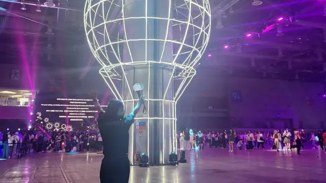 이연수 씨가 아미밤 구조물 앞에서 응원봉을 든 손을 들고 있다