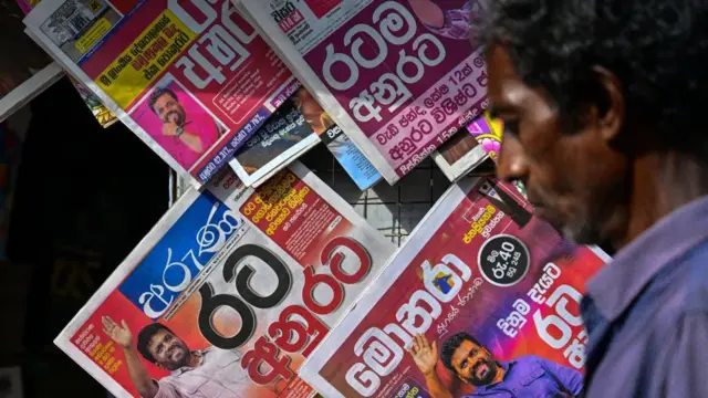 2024 සැප්තැම්බර් 23 වන දින කොළඹදී, රටේ ජනාධිපතිවරණ ප්‍රතිඵලවල මුල් පිටු සහිතව විකිණීමට තබා ඇති ශ්‍රී ලාංකික පුවත්පත් සහිත කුටියක් පසුකර යන මිනිසෙක්.