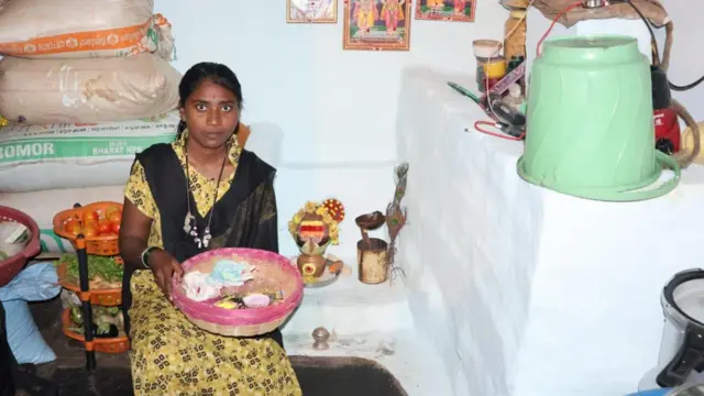 Ankita evində oturub, dizində bambuk səbət tutur. Arxasında tərəvəz qabları, divarları isə tanrıların şəkilləri ilə bəzədilib.