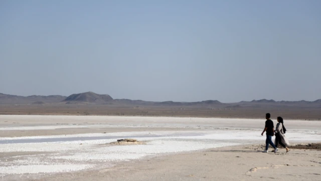 رجل وامرأة يمشيان على قاع بحيرة حوض سلطان في منطقة قُم – ويمكن رؤية الملح على سطح القاع"