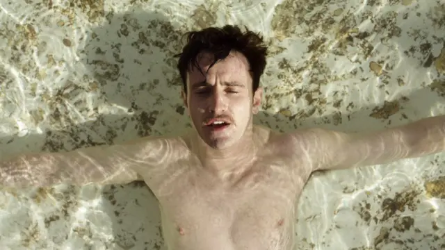 Paul Mescal with his arms out, seen from above in shallow water