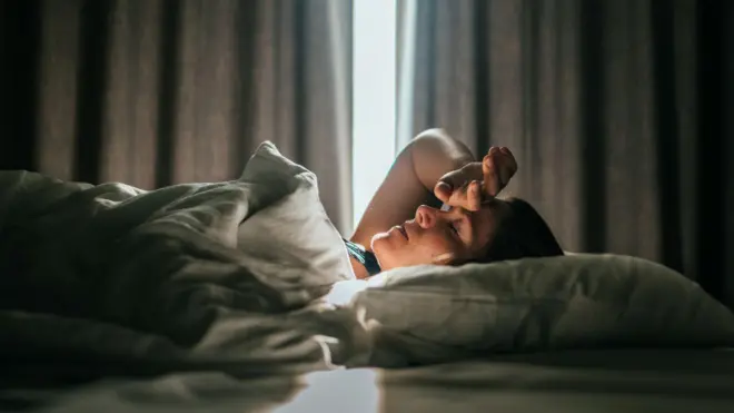 yatakta uyumaya çalışan bir kadın, kapalı perdeler arasından sızan ışıkta