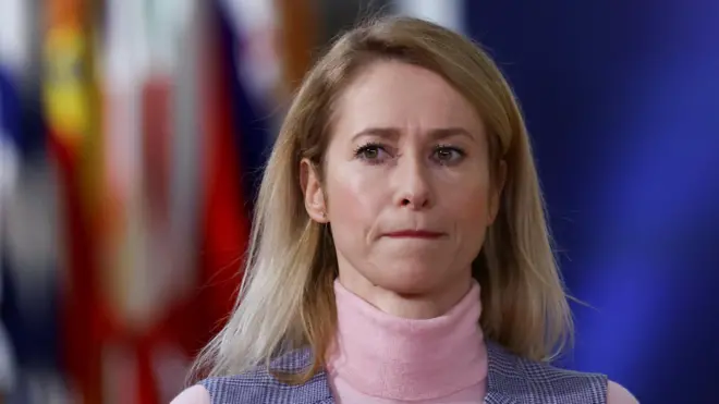 肩までの長さのブロンドの髪をした女性で、カメラから少し目をそらしている。眉間にしわを寄せ、口をぎゅっと閉じている。ピンクのタートルネックを着ている