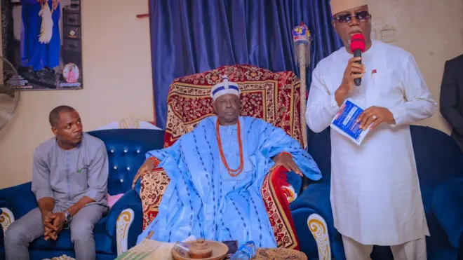 Gomina Lucky Aiyedatiwa to wọ asọ toke tilẹ alawọ funfun, de fila, o si mu iwe kan lọwọ. O n sọrọ ni ẹba itẹ Ọba Imafon, ẹni to wọ asọ agbada leesi alawọ buluu, o de ade, o si lo ilẹkẹ. Bakan naa, ẹnikan joko sori aga ni ọwọ ọtun ọba naa